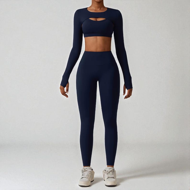 May include: Navy blue activewear set. The set includes a long-sleeved crop top with a keyhole cutout, a matching sports bra, and high-waisted leggings. The outfit is made of a smooth, stretchy material, perfect for workouts or casual wear.
