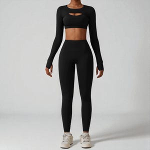 May include: A black athletic outfit consisting of a long-sleeved crop top with a chest cutout, a sports bra, and high-waisted leggings. The outfit is made of a stretchy material and is designed for workouts.
