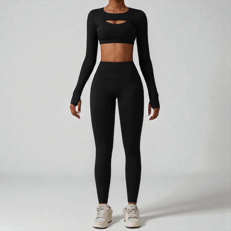 May include: A black athletic outfit consisting of a long-sleeved crop top with a chest cutout, a sports bra, and high-waisted leggings. The outfit is made of a stretchy material and is designed for workouts.