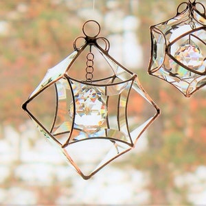 May include: Two iridescent glass cube ornaments with crystal prisms hanging from a wire. The cubes are made of clear glass with a copper wire frame.