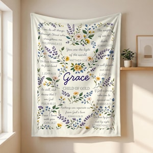 Pode incluir: Um cobertor creme com design floral e de escrita. O cobertor apresenta a palavra "Grace" no centro, rodeada por arranjos florais e versículos bíblicos. O texto inclui "Child of Gold".
