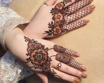 May include: Close-up of hands decorated with detailed henna patterns. The henna art showcases floral designs, including large flowers and delicate vines, in shades of brown. The fingers are decorated with lattice-like patterns, and the nails are painted a warm brown.