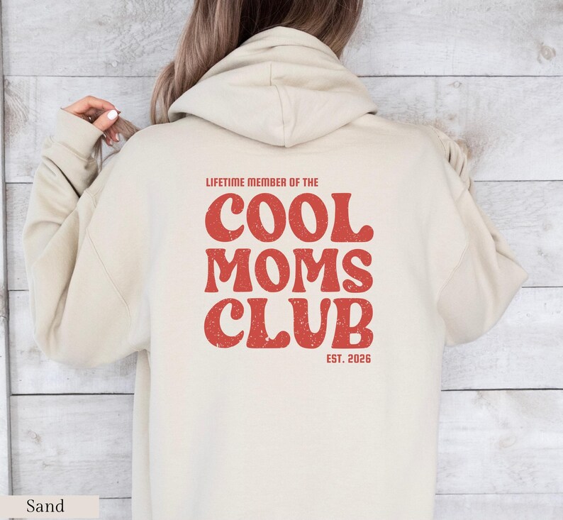 May include: Sand-colored hoodie with the text "LIFETIME MEMBER OF THE COOL MOMS CLUB EST. 2026" in red, retro-style lettering. The hoodie features a hood and long sleeves, perfect for casual wear.