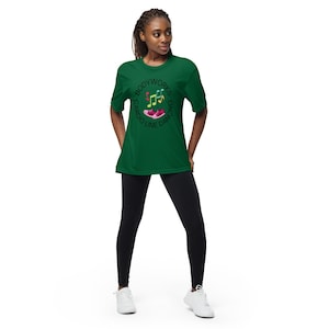 May include: A green t-shirt with the words "BODYWORKS CARDIO LINE DANCING" in a circular design. The design includes musical notes and a pink shoe. The person is wearing black leggings and white trainers.
