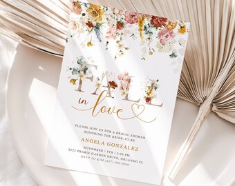 May include: Fall in love bridal shower invitation with floral design. The invitation features a watercolor floral garland with a gold script font that says "Fall in love" with a heart. The text includes the bride-to-be's name, date, time, and location. RSVP information is also included.