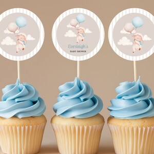 Peut inclure: Trois cupcakes bleus et blancs avec un glaçage blanc en spirale. Chaque cupcake est surmonté d'un papier rond rayé gris et blanc avec un agneau de dessin animé tenant des ballons. Le topper du milieu porte le texte "Baby Shower d'Everleigh".