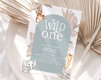 May include: A light blue invitation card with the text "Wild One" in gold lettering. The card features illustrations of a monkey, elephant, and giraffe, along with tropical leaves. The text on the card reads "Please join us to celebrate Amelia's First Birthday".