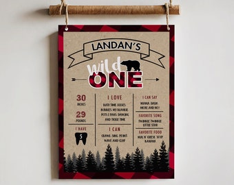 Puede incluir: Un póster imprimible de cuadros marrones y rojos con una silueta de oso negro y el texto "Landan's Wild One". El póster incluye detalles sobre la edad, la altura, el peso y las cosas favoritas del niño.