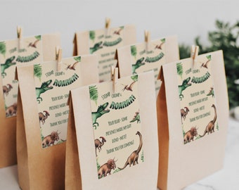 May include: Brown paper bags with green and white dinosaur-themed party favor tags. The tags feature a dinosaur with the text "Stomp Chomp & Roar!" and "Your roar-some presence made my day Dino-mite! Thank you for coming!"