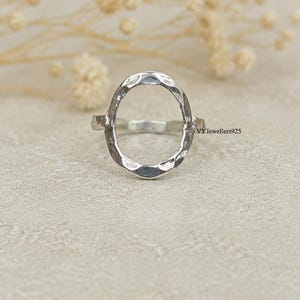 Op de afbeelding: Een zilveren ring met een groot, open ovaalvormig middendeel met een gehamerde, getextureerde afwerking. De ringband is dun en glad en verbonden met de zijkanten van het ovaal. De tekst VYJewellers925 is zichtbaar aan de rechterkant van de ring.