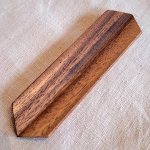 May include: A wooden, angled display stand with a natural wood grain pattern. The stand is a warm brown color and has a V-shaped design. The stand is likely used for displaying items.