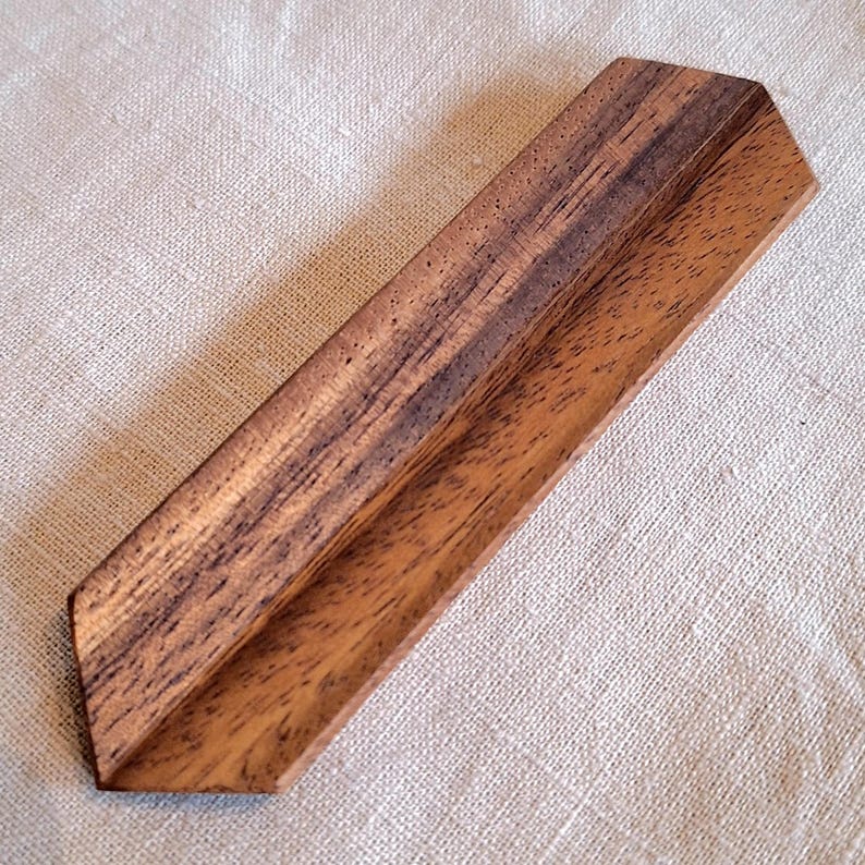 May include: A wooden, angled display stand with a natural wood grain pattern. The stand is a warm brown color and has a V-shaped design. The stand is likely used for displaying items.