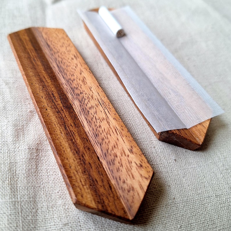 May include: A wooden rolling tray set with a natural wood grain finish. The set includes a tray and a matching lid. A white rolling paper with a rolled cigarette is on the tray.
