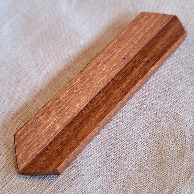 May include: A handcrafted wooden incense holder with a rich, reddish-brown finish. The rectangular tray features a central groove for holding incense sticks. The holder's angled edges and natural wood grain add to its rustic charm.