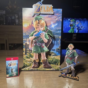 Peut inclure: Un ensemble de présentation comprenant une toile de fond rectangulaire verticale avec l'image imprimée de Link jouant de l'ocarina, une figurine de Link tenant une épée sur un socle, et un boîtier de jeu The Legend of Zelda: Ocarina of Time.