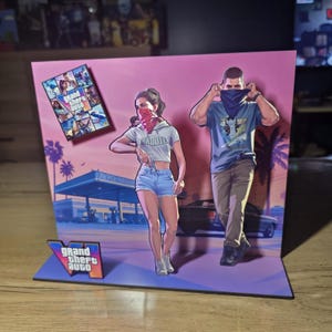 Peut inclure: Un présentoir en relief 3D illustrant Grand Theft Auto. Il représente deux personnages, l'un en haut court blanc et short en jean avec un bandana rouge, l'autre en t-shirt bleu et pantalon beige avec un bandana bleu, devant une station-service.