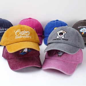 May include: A collection of colorful baseball caps in various shades, including yellow, blue, pink, and gray. Some caps feature embroidered designs and text, such as "Custom Embroidery," a dog logo, and "Children name."