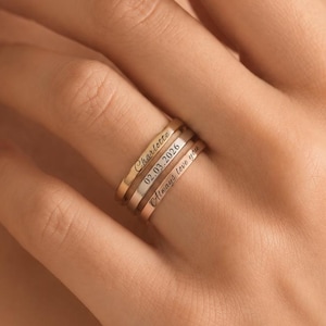 Può includere: Un set di tre anelli sottili in metallo sovrapposti nei toni dell'oro rosa, dell'argento e dell'oro. Ogni anello presenta una superficie piatta con un'incisione personalizzata. L'anello superiore riporta il nome Charlotte, quello centrale 02.03.2026 e quello inferiore Always love you.