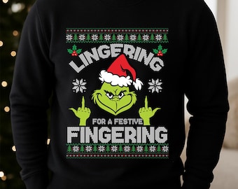May include: Black sweatshirt with a Grinch design wearing a Santa hat and giving the middle finger. The text reads "LINGERING FOR A FESTIVE FINGERING" in white. The design includes snowflakes and Christmas tree patterns.