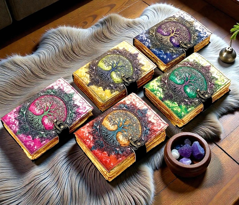 Puede incluir: Una colecci&oacute;n de diarios decorativos con dise&ntilde;os de &aacute;rbol de la vida. Cada diario presenta una combinaci&oacute;n de colores diferente, incluyendo rosa, amarillo, azul, verde y rojo. Los diarios tienen cierres de metal ornamentados y bordes dorados. Tambi&eacute;n hay un peque&ntilde;o cuenco de madera con cristales.