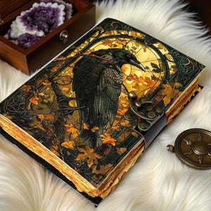 May include: A decorative journal with a raven illustration on the cover, featuring a brass clasp and aged-look pages. The cover art includes autumn leaves and a stained-glass style background. A small compass is next to the journal.