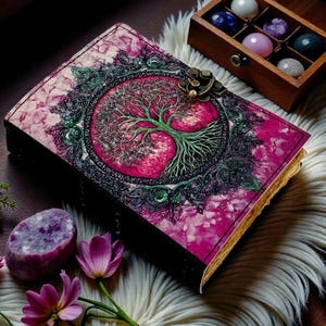 Puede incluir: Un diario decorativo con un dise&ntilde;o de &aacute;rbol de la vida rosa y verde en la portada. El diario tiene un cierre de metal y est&aacute; rodeado de cristales y flores. La portada del diario es de un color rosa y verde vibrante.