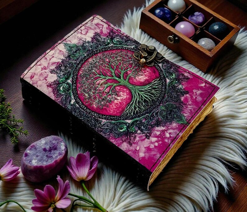 Puede incluir: Un diario decorativo con un dise&ntilde;o de &aacute;rbol de la vida rosa y verde en la portada. El diario tiene un cierre de metal y est&aacute; rodeado de cristales y flores. La portada del diario es de un color rosa y verde vibrante.