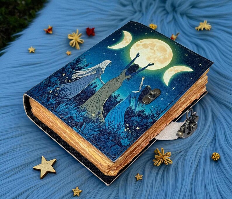 Puede incluir: Un diario encuadernado en cuero con un dise&ntilde;o celestial. La portada presenta una escena nocturna con tres figuras que se extienden hacia una luna llena y medias lunas. El diario tiene un cierre de metal y p&aacute;ginas envejecidas. Estrellas y flores decorativas rodean el diario.