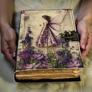 May include: A decorative journal with a fairy design. The cover features a fairy in a purple dress with lavender flowers and wings. The journal has a metal clasp and aged paper pages.