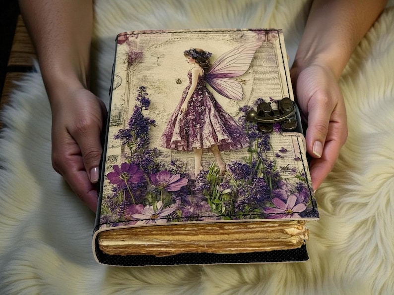 May include: A decorative journal with a fairy design. The cover features a fairy in a purple dress with lavender flowers and wings. The journal has a metal clasp and aged paper pages.