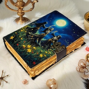 May include: A decorative journal with a dark blue cover depicting skeletons dancing under a full moon. The journal has aged pages and a metal clasp. The cover art includes yellow flowers and a starry sky. The pages appear to be aged.