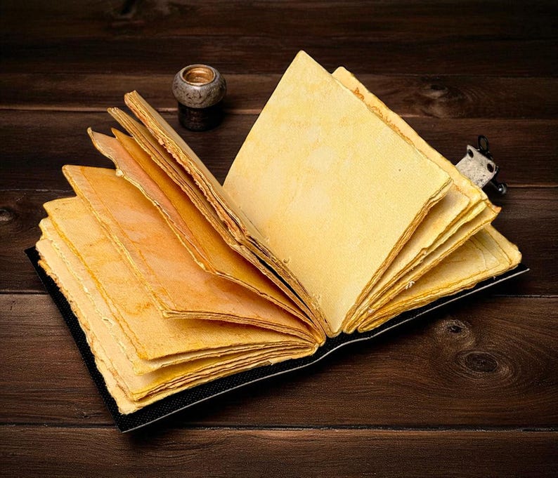 Puede incluir: Un diario abierto de estilo antiguo con p&aacute;ginas amarillentas y envejecidas. El libro est&aacute; encuadernado en negro y descansa sobre una superficie de madera oscura. Un peque&ntilde;o candelabro decorativo es visible en el fondo, lo que a&ntilde;ade a la est&eacute;tica vintage.