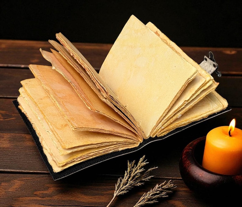 Puede incluir: Un diario abierto de estilo antiguo, con p&aacute;ginas amarillentas y envejecidas. Se ve un peque&ntilde;o marcap&aacute;ginas decorativo. Una vela naranja encendida en un portavelas de madera est&aacute; cerca, con ramitas de plantas secas en primer plano. El diario est&aacute; sobre una superficie de madera oscura.