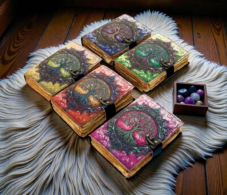 Puede incluir: Una colecci&oacute;n de cinco diarios encuadernados en cuero con cubiertas coloridas que presentan un dise&ntilde;o de &aacute;rbol de la vida. Cada diario tiene un cierre de metal y p&aacute;ginas envejecidas. Los diarios est&aacute;n colocados sobre una alfombra blanca y esponjosa.