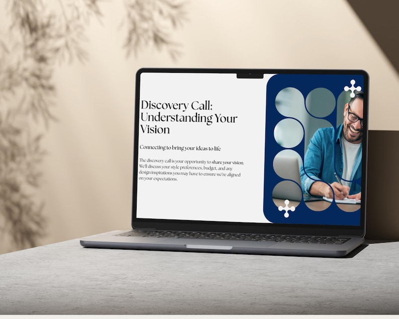 May include: A laptop displaying a presentation titled "Discovery Call: Understanding Your Vision." The screen shows text and an image of a man smiling and writing. The laptop is open on a light gray surface.