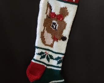 May include: Hand-knitted Christmas stocking with a reindeer design. The stocking is primarily white with red, green, and brown accents. The name "GABEE" is knitted in red letters at the top. The reindeer has a red bow and a red nose.