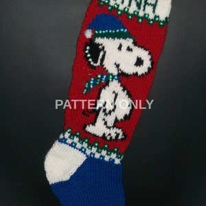 May include: Red and white knitted Christmas stocking with a blue and green trim. The stocking features a white Snoopy character with a blue hat and a green scarf. The stocking is decorated with green and white sequins and the name "Nina" is knitted into the top of the stocking.