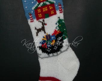 May include: A white knitted Christmas stocking with a blue and white striped cuff. The stocking features a red house with a green roof, a reindeer pulling a sleigh with presents, and a green Christmas tree. The stocking is decorated with white snowflakes and silver glitter.