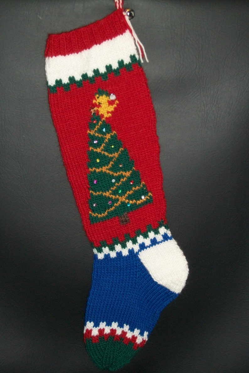 May include: A red, white, blue, and green knitted Christmas stocking with a green Christmas tree design and a bell at the top.