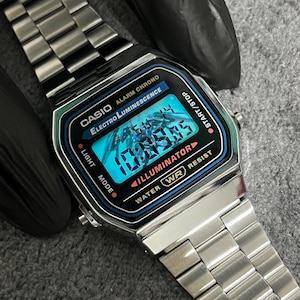 Puede incluir: Reloj digital Casio plateado con esfera negra y azul que muestra la hora. El reloj tiene una correa de acero inoxidable y presenta el texto "CASIO ALARM CHRONO ELECTRO LUMINESCENCE". La esfera del reloj muestra la hora 10:09:05.