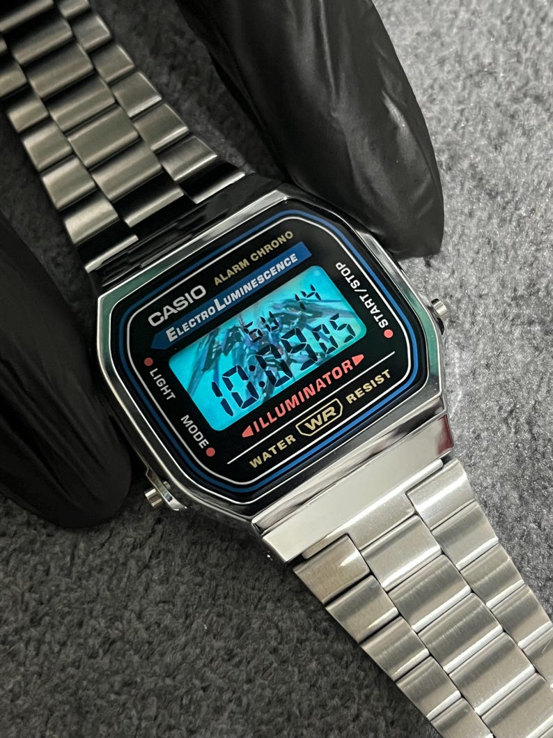 Puede incluir: Reloj digital Casio plateado con esfera negra y azul que muestra la hora. El reloj tiene una correa de acero inoxidable y presenta el texto "CASIO ALARM CHRONO ELECTRO LUMINESCENCE". La esfera del reloj muestra la hora 10:09:05.
