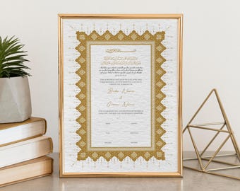 Puede incluir: Un certificado de boda enmarcado con bordes y texto dorados ornamentados. El certificado tiene un fondo blanco texturizado y texto dorado. El marco es dorado. Una pequeña planta en maceta y libros están a la izquierda, y una escultura geométrica dorada está a la derecha.