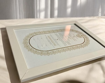 Puede incluir: Un certificado enmarcado en blanco con un borde de filigrana dorada. El certificado tiene un fondo azul claro y texto en una fuente de escritura. El marco es rectangular y tiene un acabado mate. El certificado se muestra sobre una superficie blanca.