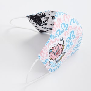 May include: White face mask with a pink and blue donut character skateboarding on a white background with blue and pink swirls. The text "Donut Apparel" is visible on the other side of the mask.