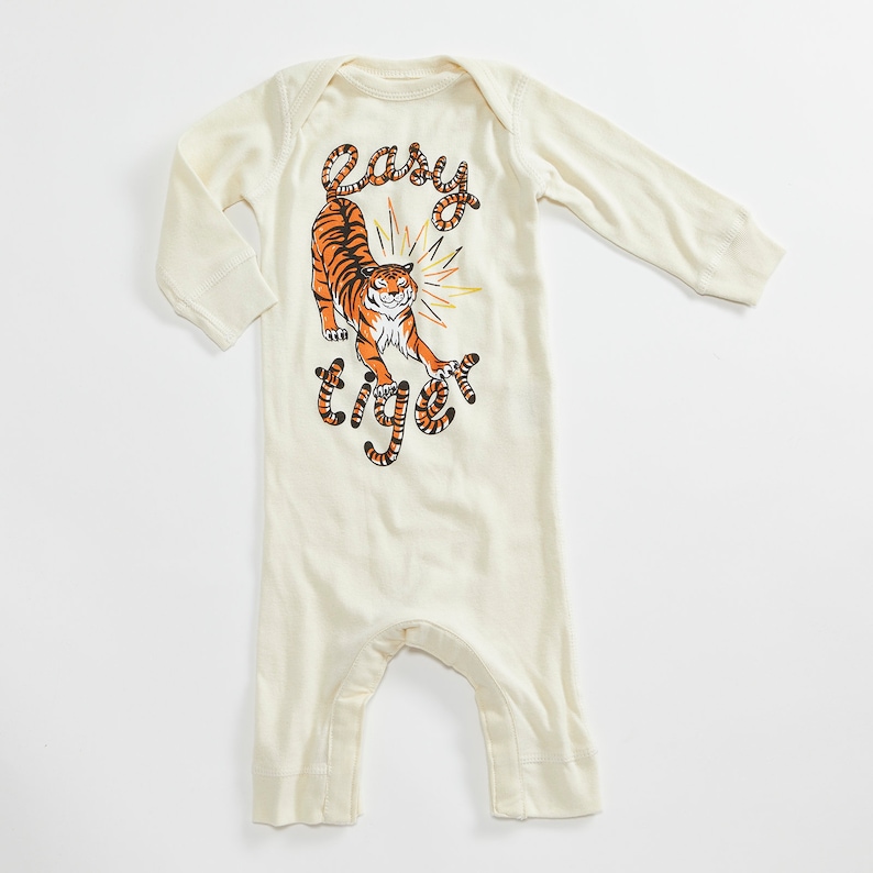 May include: A cream-colored long-sleeved baby onesie with a graphic of a tiger and the text "easy tiger".