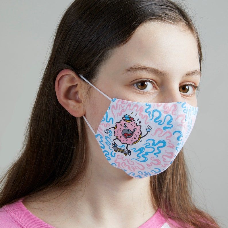 May include: A white face mask with a pink and blue donut character wearing a hat and skateboarding on a blue and pink swirl pattern.