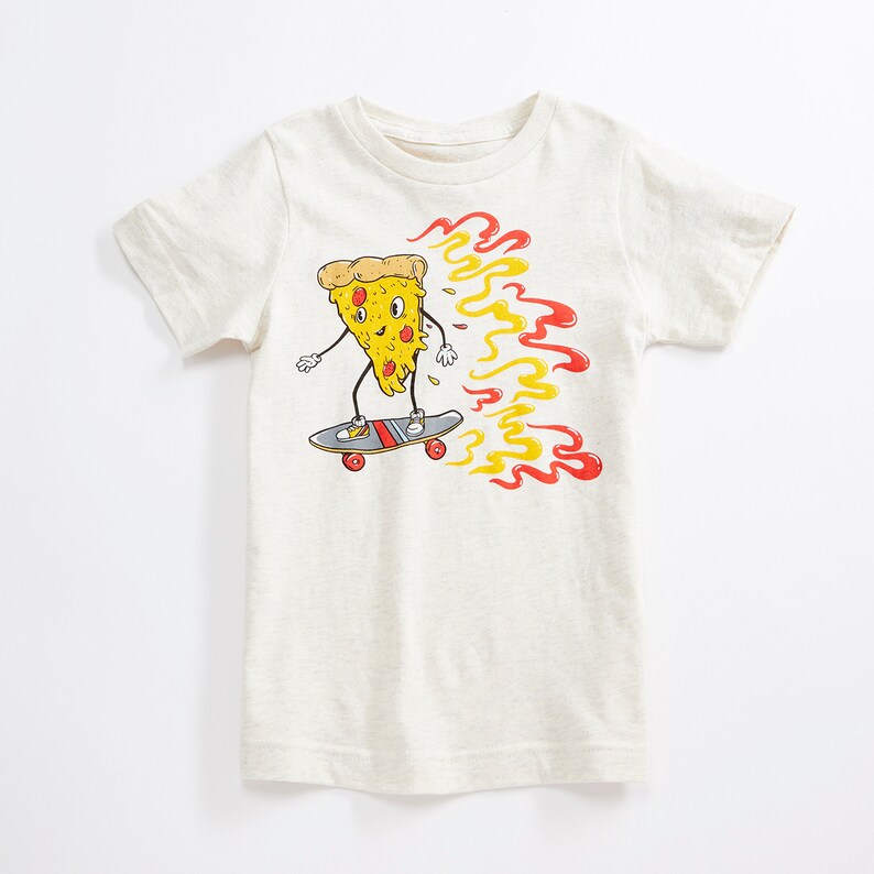 Puede incluir: Una camiseta blanca con un gr&aacute;fico de una rebanada de pizza en una patineta con llamas detr&aacute;s. La rebanada de pizza tiene una cara y lleva zapatos.