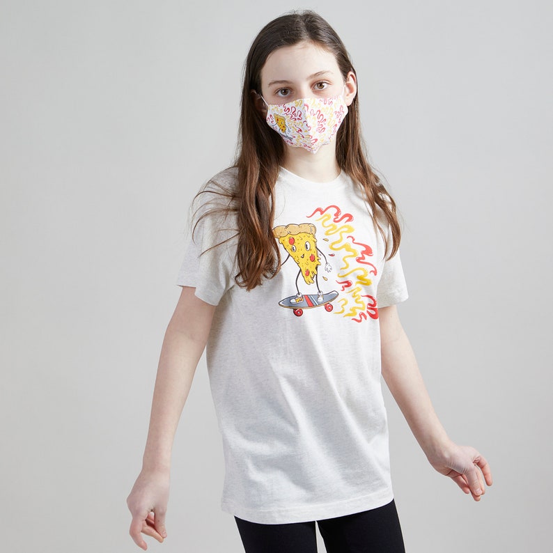 Puede incluir: Una camiseta blanca con un gr&aacute;fico de una rebanada de pizza en una patineta con llamas. La rebanada de pizza tiene una cara y lleva zapatos rojos. La persona que lleva la camiseta lleva una mascarilla blanca con un patr&oacute;n de pizza.