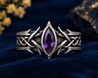 May include: A silver-toned metal ring featuring a central marquise-cut purple gemstone. The band displays an intricate, textured knotwork pattern and pointed, thorn-like metal accents extending from the center setting.