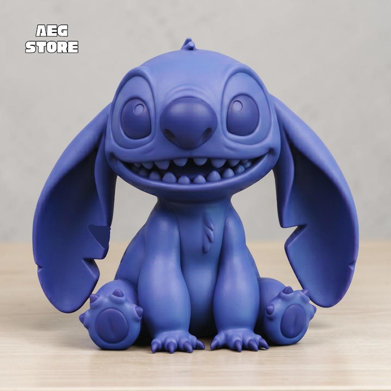 May include: A blue figurine of the character Stitch from the Disney movie Lilo & Stitch. The figurine is in a seated position with a large grin, large ears, and four legs. The text "AEG STORE" is in the upper left corner.